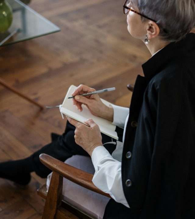 pexels-photo-4098148-4098148 A professional woman with glasses taking notes while seated indoors, depicting consultation or therapy.