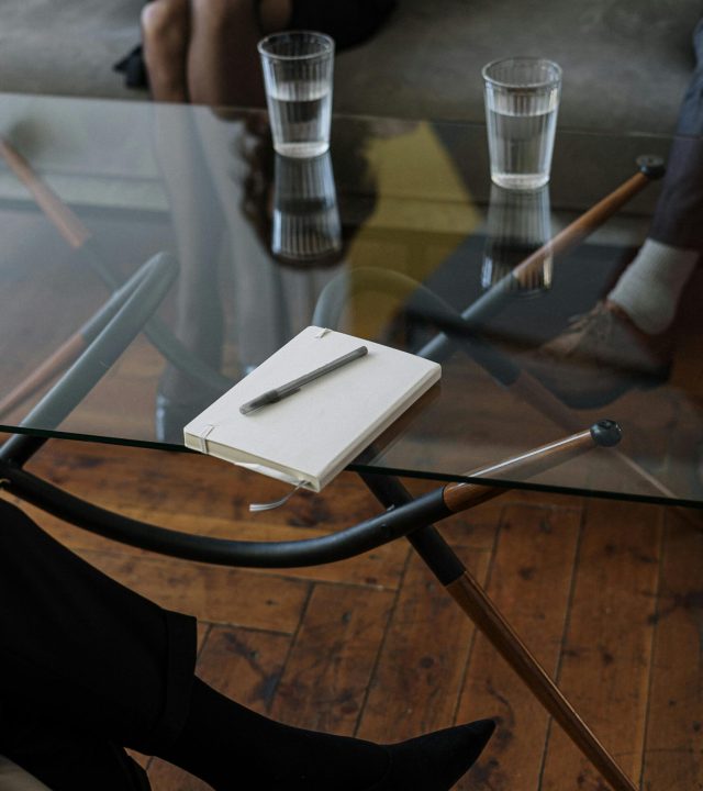 pexels-photo-4098232-4098232 Close-up of a counseling session with two glasses of water and a notepad on a glass table.